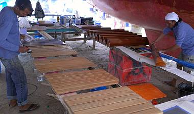 Baw epoxying the slatted floorboard while Lek sands bookshelves